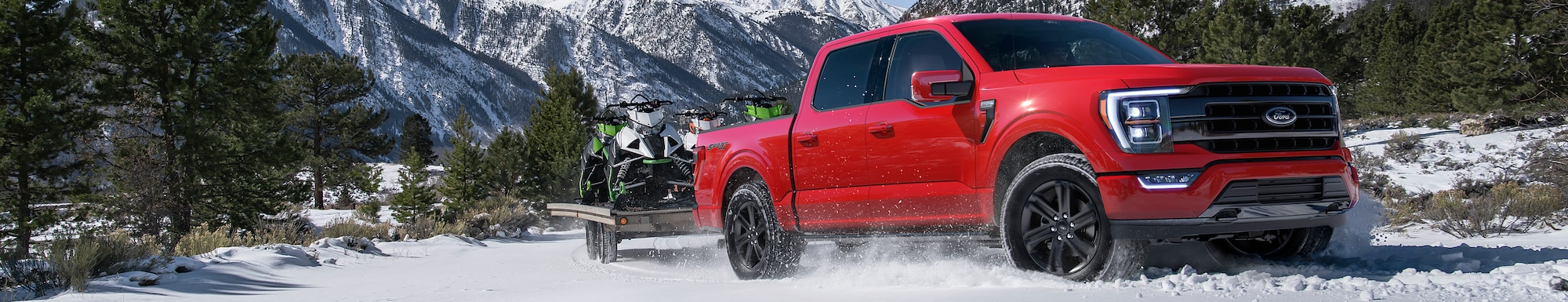 Red Truck Towing Snowmobiles Infront of Snowy Mountains
