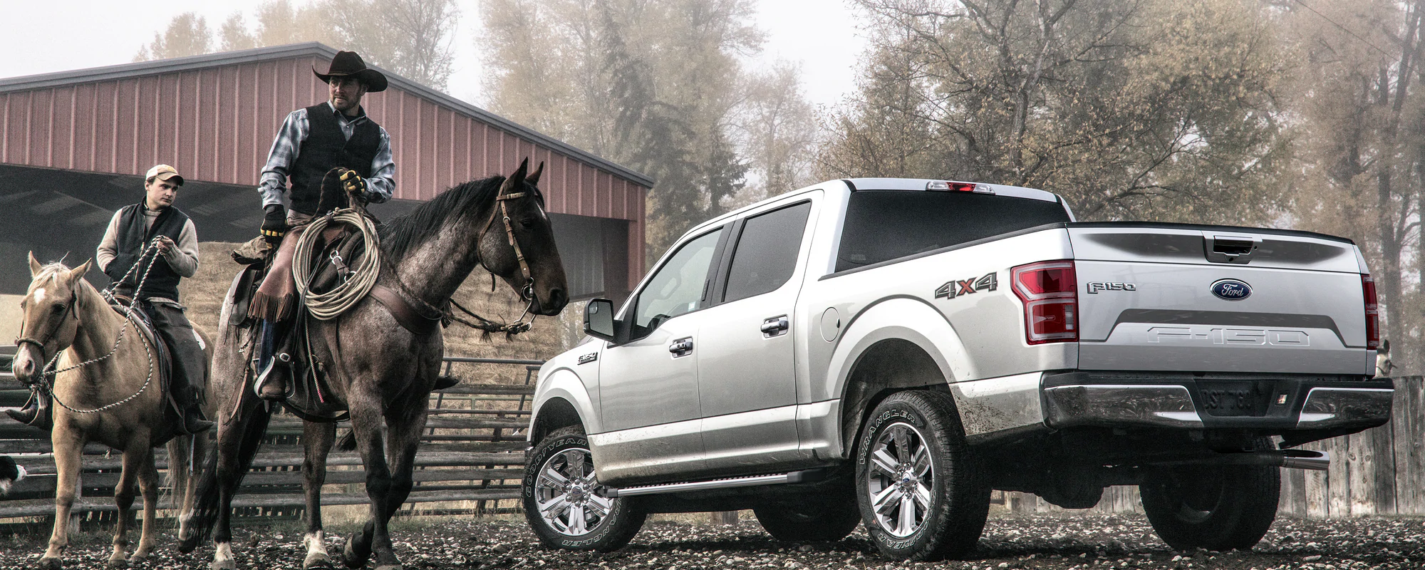 Silver Ford Truck in front of a barn next to two men riding horses